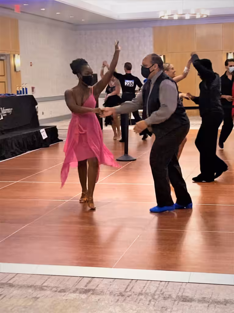 Four elegantly-dressed couples are dancing at a ballroom event.