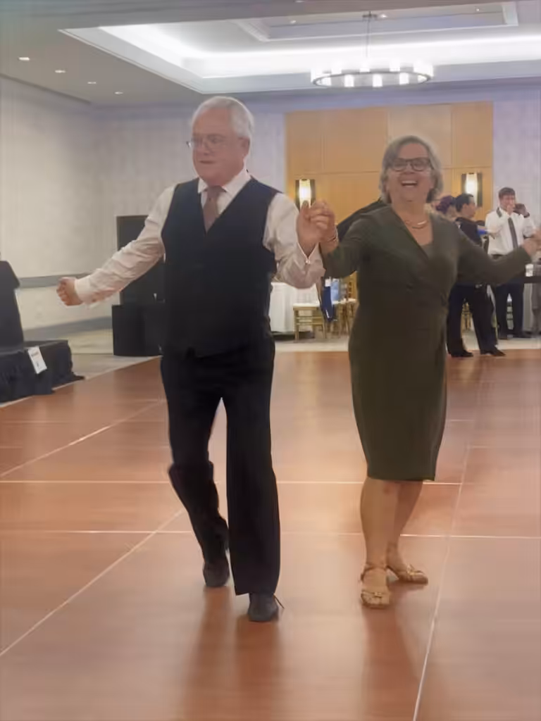 A happy senior couple dance in formal attire at an indoor ballroom event.