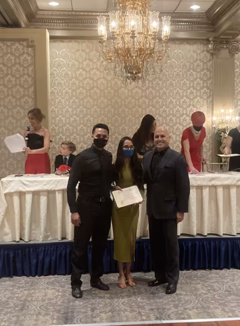 Two men and a women posing for a picture at a formal indoor event under a chandelier.