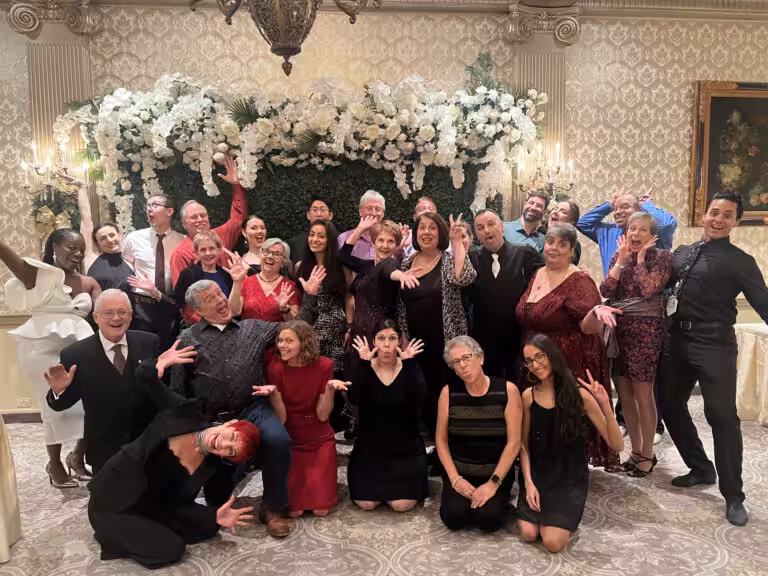 Many people pose for a picture in front of a flower-decorated wall at a ballroom.