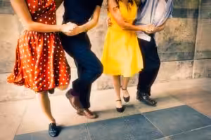 Two couples in colorful clothing seen from shoulders down are dancing.