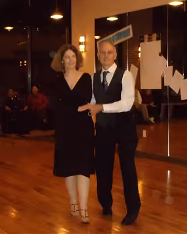 A middle-aged couple in formal clothing partake at a dance event.