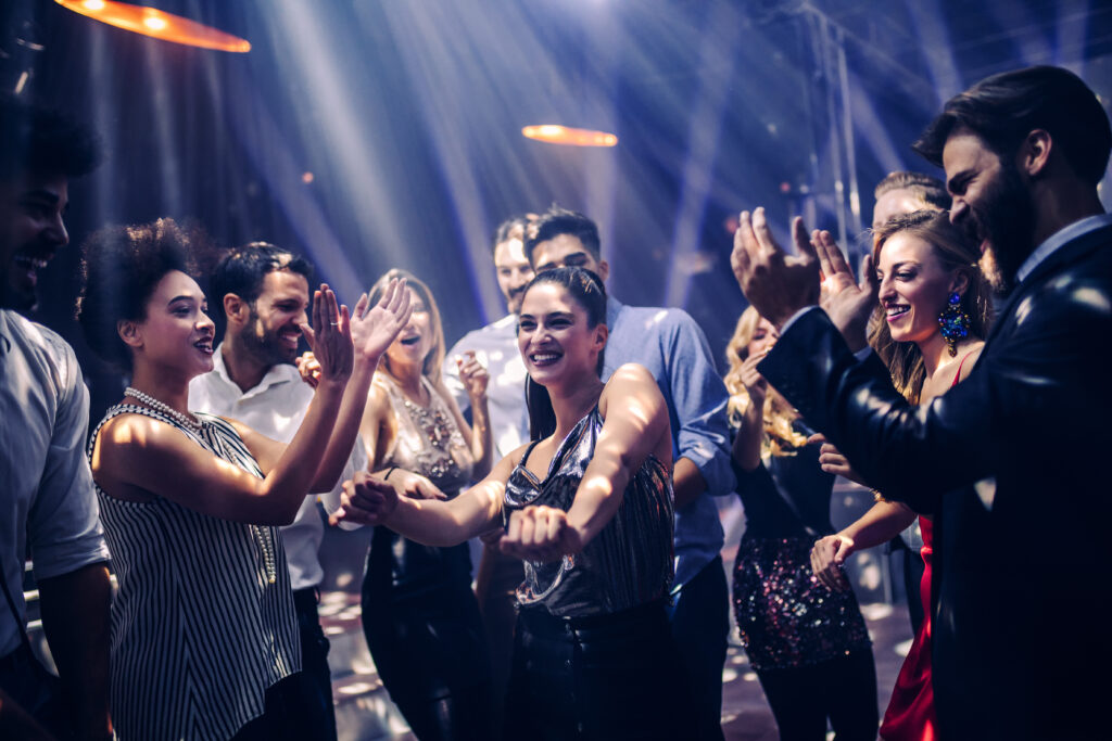 A diverse group of men and women dance together at a nightclub, laughing and enjoying themselves.