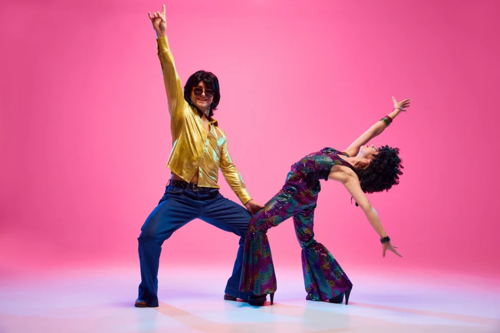 A disco-themed couple strikes a pose. The man has a gold shirt and the woman wears a sequined outfit.