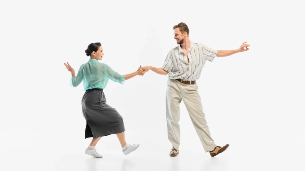 A man in a striped shirt and khakis dancing swing or rock-and-roll with a woman in a green blouse and gray skirt.