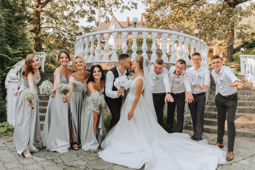 Bride and groom kissing with wedding party outdoors